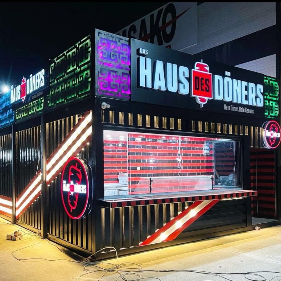 Haus des Döners – LED-Foodcontainer mit Verkaufsfenster Gastronomiecontainer mit LED-Fassade bei Nacht – Haus des Döners mit Glas-Front, rotem Fliesendesign und Verkaufsmodul
